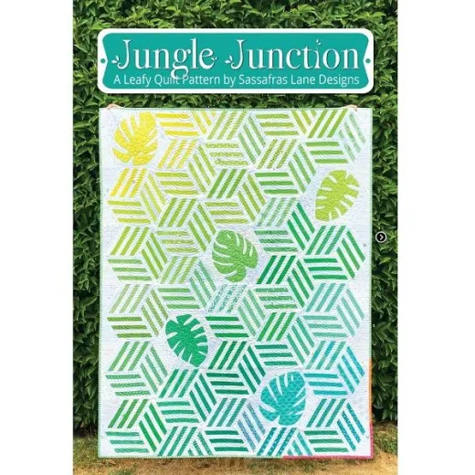 Jungle Junction Titelbild Fertiger Quilt mit gestreiften Hexagon-Blöcken in Grün- und Gelbtönen und applizierten Monstera-Blättern, vor einer Hecke aufgehängt.